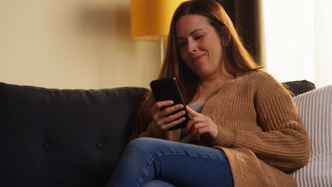 Woman-Sitting-On-Sofa-At-Home-At-Streaming-Or-Watching-Movie-Or-Show-Or-Scrolling-Internet-On-Mobile-Phone-10